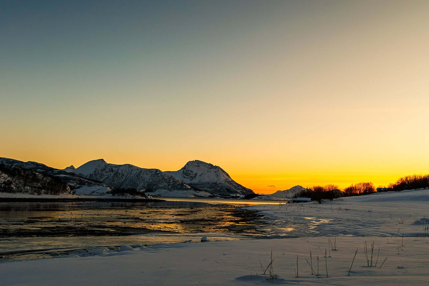 Solnedgang over snødekt landskap med fjell og islagt fjord, som skaper en harmonisk vinterstemning.