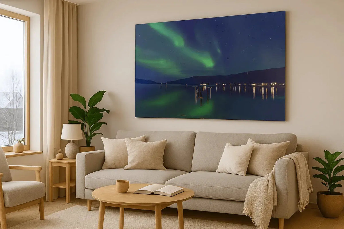 Veggbilde av Nordlys som lyser opp en stille fjord i moderne stue med sofa og planter.