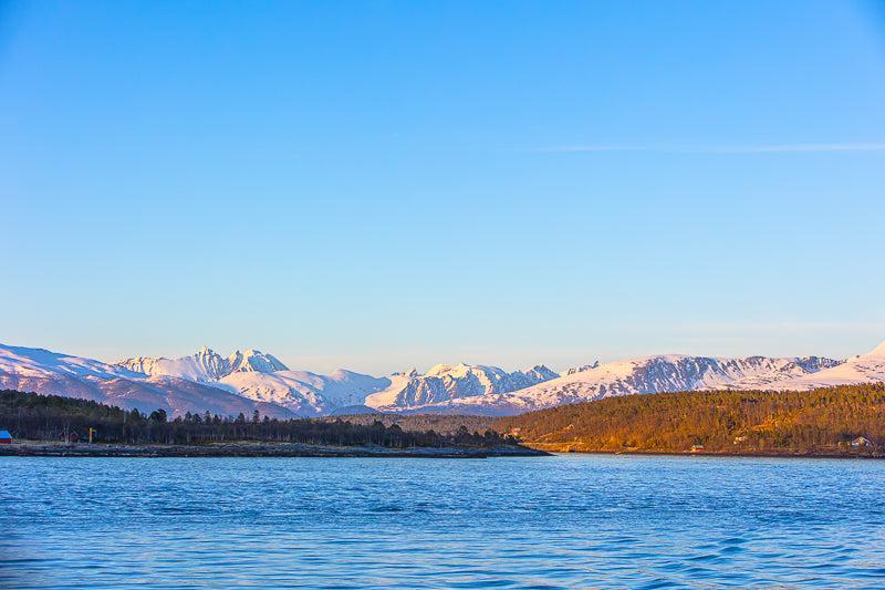 Arktisk landskap med snødekte fjell og rolig hav ved Tromsø, som gir en følelse av arktisk natur.