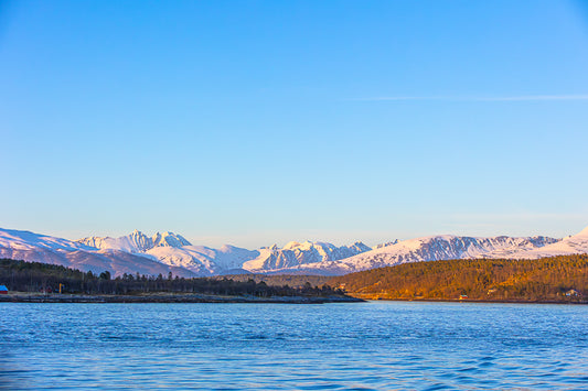Arktisk landskap med snødekte fjell og rolig hav ved Tromsø, som gir en følelse av arktisk natur.