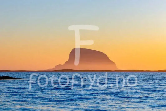 Lovund i solnedgang med hav og gyllent lys, majestetisk fjellprofil i horisonten.
