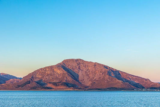 Lysinghesten-Helgeland majestetisk i varmt nordnorsk lys med havet rolig i forgrunnen.