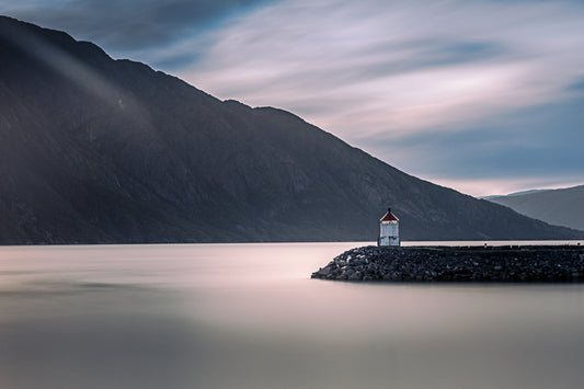 Fyrlykten ved Vefsnfjorden i Mosjøen, omgitt av fjell og speilblankt vann, skaper en rolig og nordisk atmosfære.