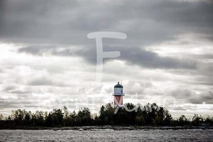 Fjärdgrund fyr med dramatisk himmel og mørkt hav, karakteristisk rødt fyrtårn over trekronene.