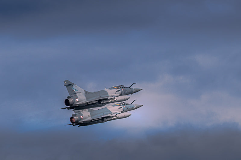 Mirage 2000 i formasjon mot en dramatisk himmel, viser fart og presisjon i luftfartsfotokunst.