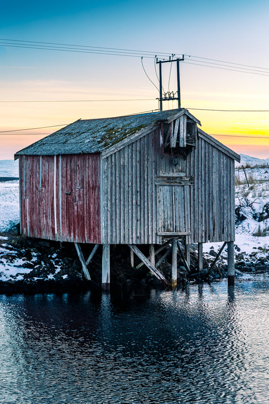 Naust i vinterlys – stemningsfullt veggbilde fra Herøy med værbitt naust ved sjøen.