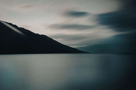 Stillhet over Vefsnfjorden med silkemykt vann og dramatiske skyer i en minimalistisk landskapsfotografi.