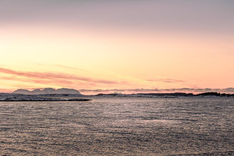 Vegafjellan sett fra Herøy med kveldslys over havet og fjell i bakgrunnen.
