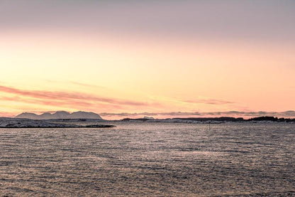 Vegafjellan sett fra Herøy med kveldslys over havet og fjell i bakgrunnen.