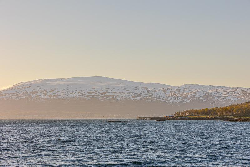 Vinterlys ved Tromsø, snødekte fjell møter havet i et rolig nordnorsk landskap.