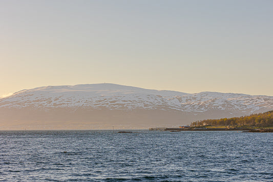 Vinterlys ved Tromsø, snødekte fjell møter havet i et rolig nordnorsk landskap.